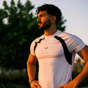 Athletic man in a white shirt stands confidently during sunrise in Jeddah, Saudi Arabia.