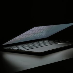 Partial view of a laptop in a dimly lit room, showcasing its sleek design and illuminated keyboard.