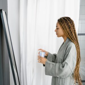 Woman in a bathrobe with braided hair gazes at her reflection in a modern minimalistic bathroom.
